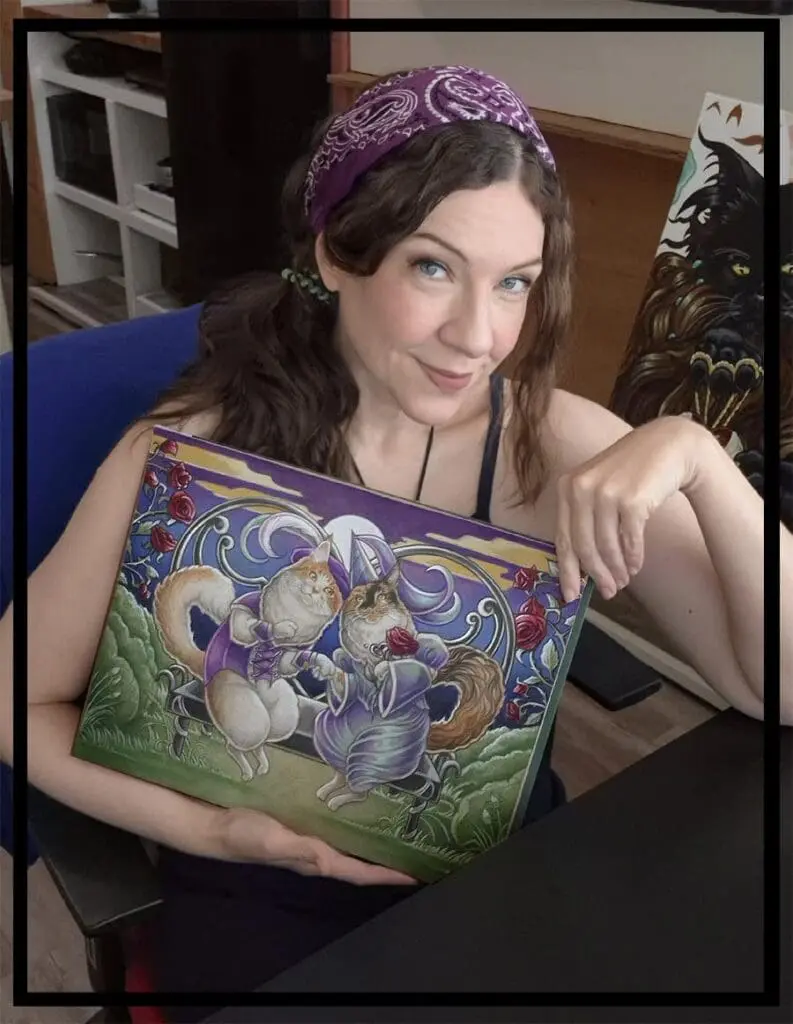 Artist Natalie Ewert holding her Romeo and Juliet Maine Coon cat artwork in her studio